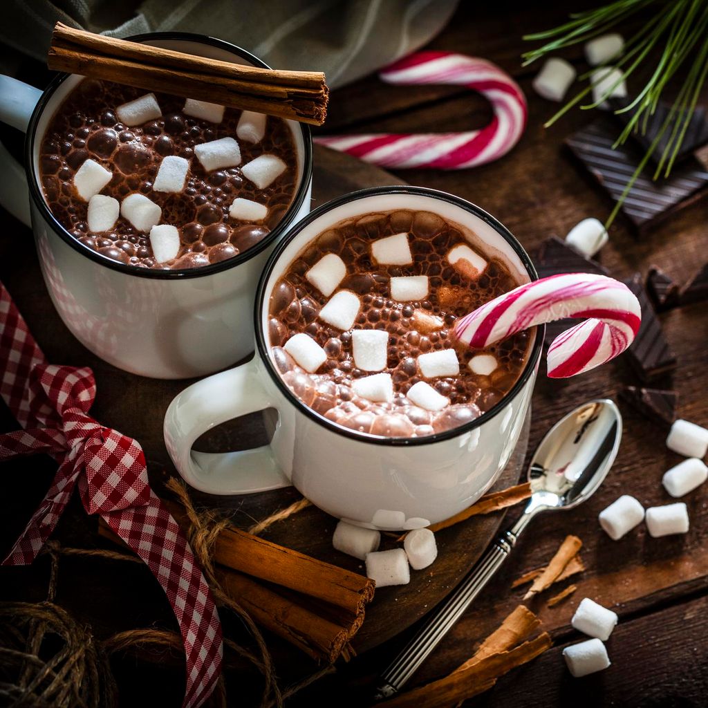 dos tazas con chocolate caliente adornada con bastoncillos navide os de caramelo malvaviscos y canela
