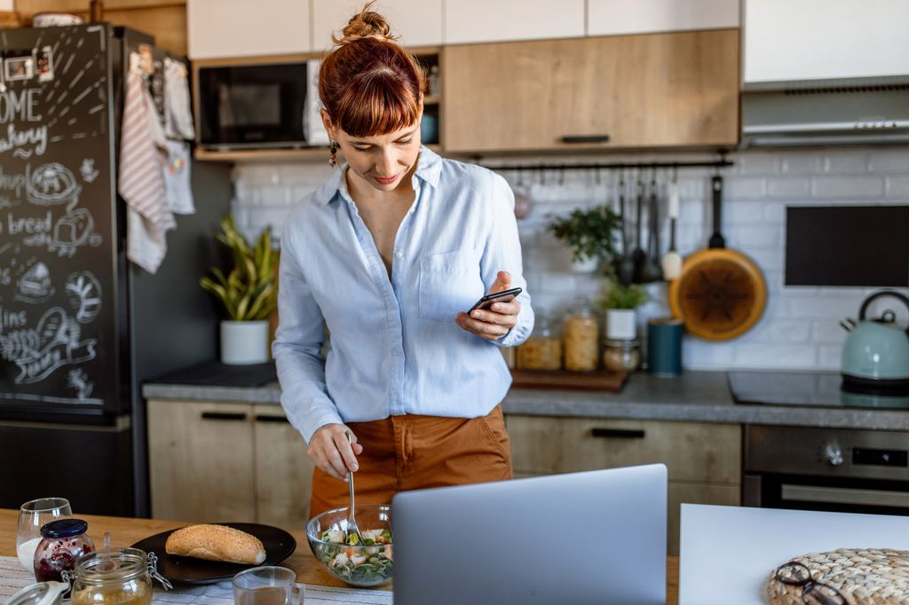 mujer muy ocupada en la cocina, con el móvil y el ordenador portátil mientras cocina