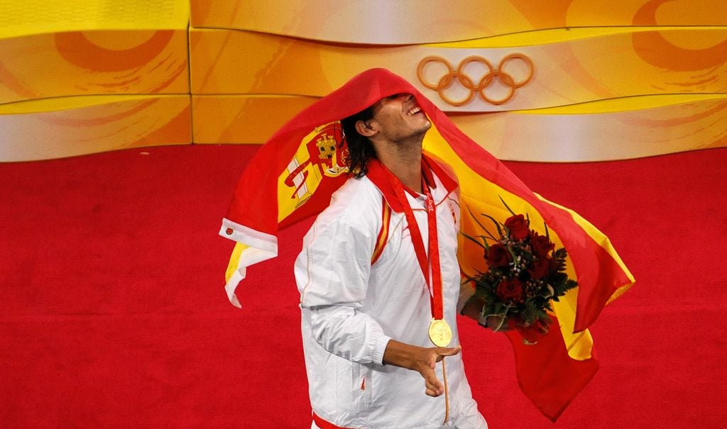 Rafael Nadal of Spain covers himself with the Spanish flag on the podium after receiving the gold medal for his victory over Fernando Gonzalez of Chile in their men's singles gold medal final tennis match during the 2008 Beijing Olympic Games on August 17, 2008. Nadal took gold with a 6-2, 7-6, 6-3 (3-0) victory. AFP PHOTO / JOE KLAMAR (Photo by Joe KLAMAR / AFP) (Photo by JOE KLAMAR/AFP via Getty Images)