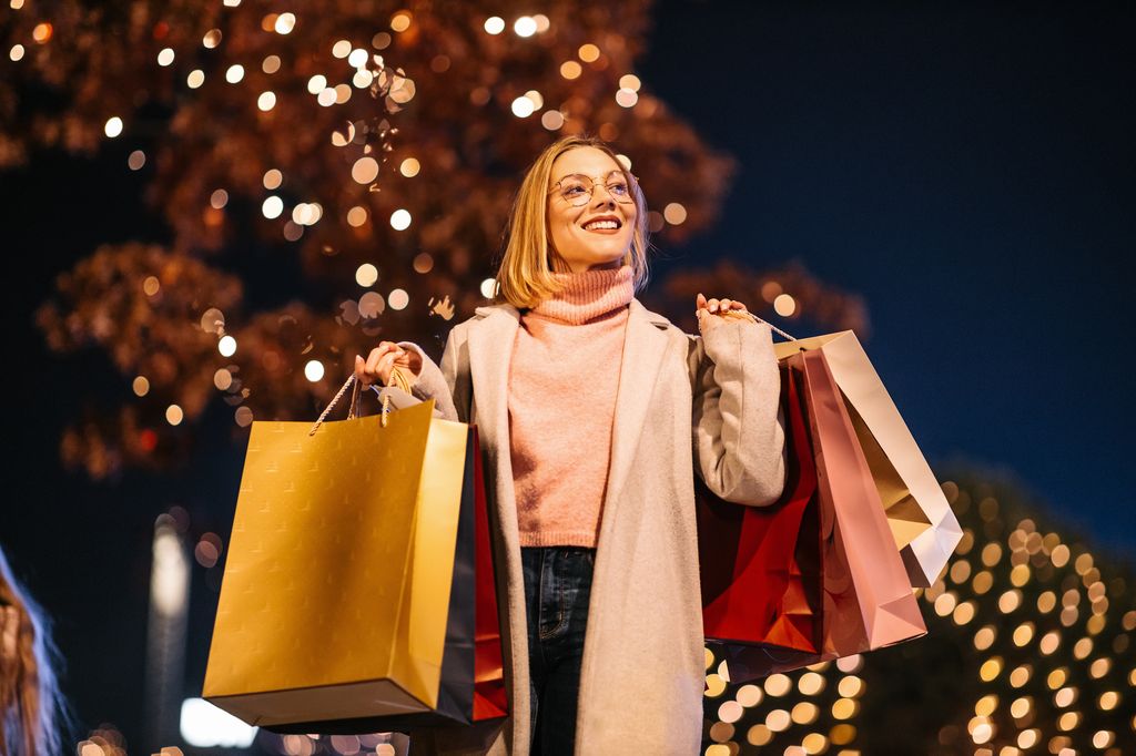 Una chica con bolsas de compra y luces navideñas de fondo