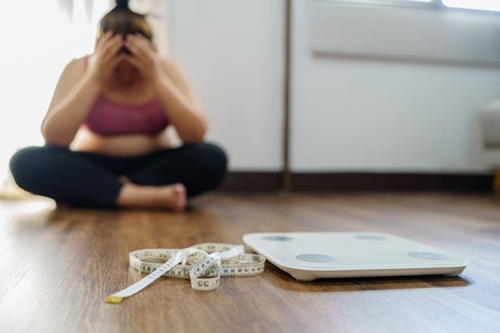 mujer triste junto a la báscula y una cinta métrica