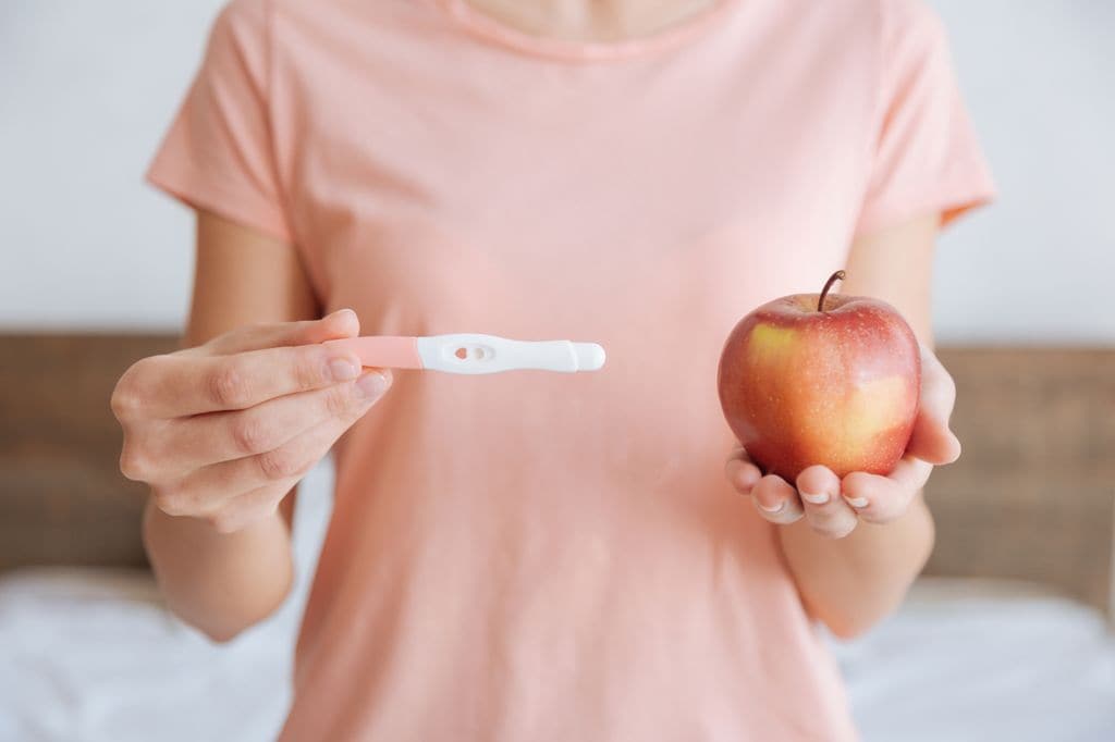 Mujer con un test de embarazo y una manzana