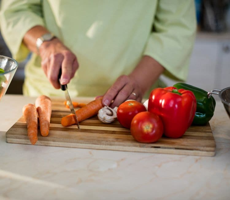 Mujer cortando verduras sobre una tabla de madera