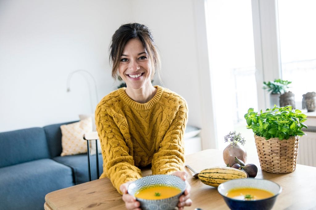 mujer sonriente con un plato de puré sobre la mesa