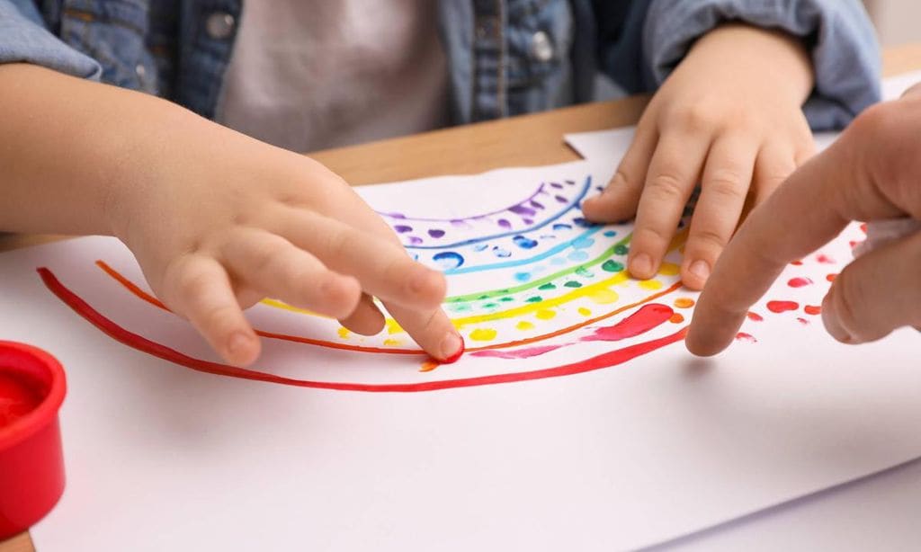 ni o pintando con los dedos un arcoiris en un folio