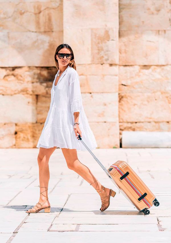 Zina Charkoplia con vestido blanco, sandalias de tiras y maleta de Samsonite