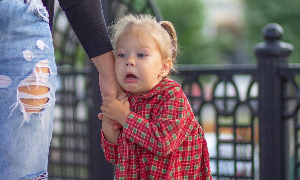 Caucasian little girl of 2 years with scared face holding hand of mother in summertime