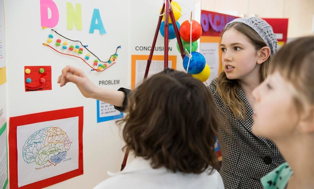 school girl explaining science fair project to classmates