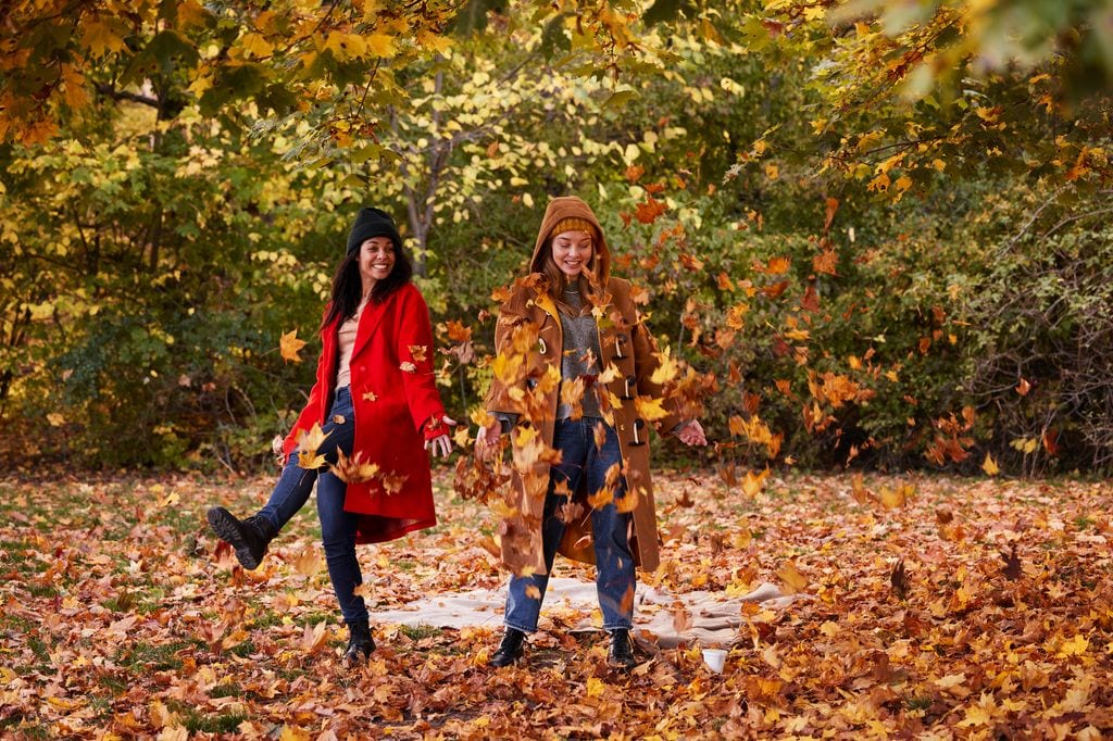 mujeres jugando con las hojas en un parque en otoño