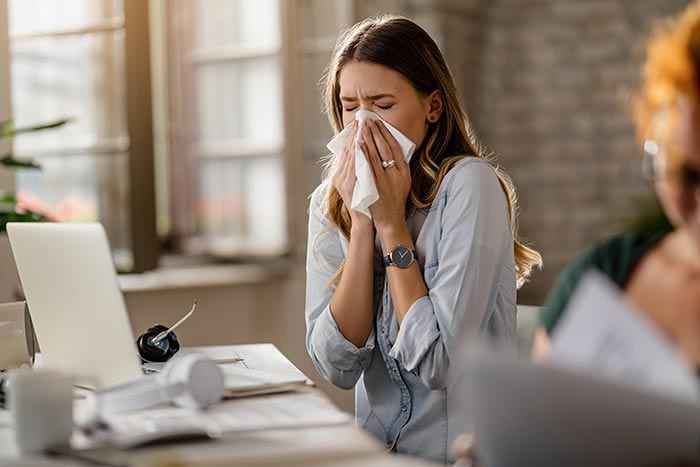 mujer estornudando en la oficina