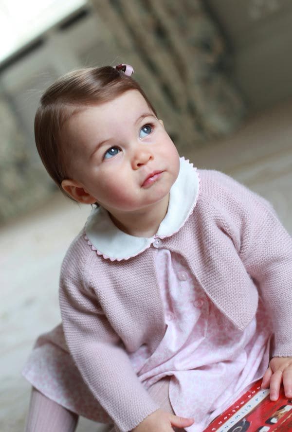 En una de las fotos, Charlotte de Cambridge está sentada aparentemente sobre el suelo alfombrado, mirando hacia arriba y sosteniendo entre las manos lo que parece ser un libro o un juguete con el dibujo de un típico autobús rojo londinense
