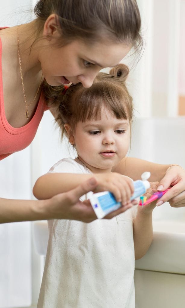 Mamá poniendo pasta de dientes en el cepillo de su hijo