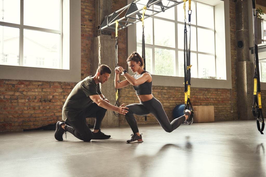 Entrenador personal ayudando a una chica que está haciendo ejercicio con un TRX en el gimnasio