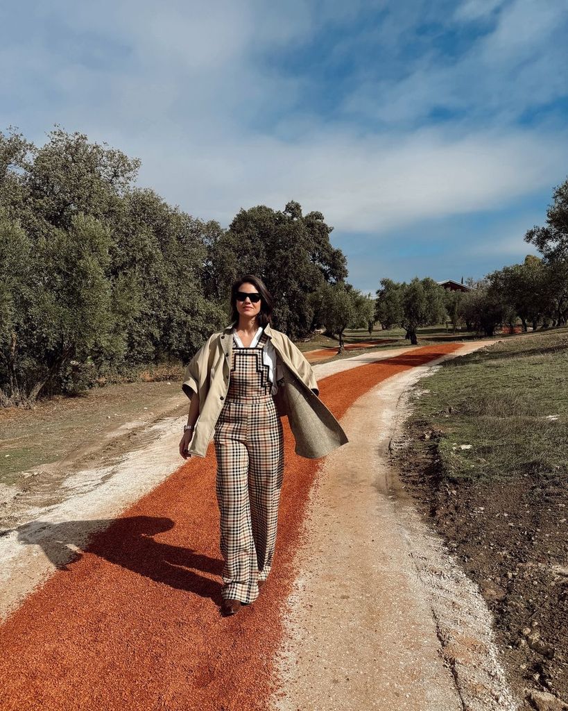 Isabelle Junot con mono de cuadros y gabardina en el campo