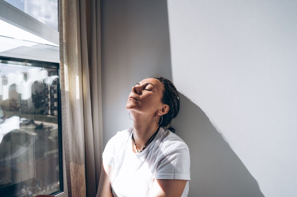 mujer pensativa, junto a la ventana, con la cabeza apoyada en la pared