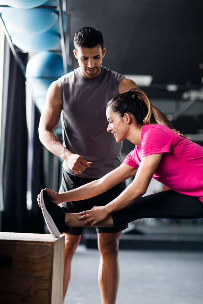 Chica estirando en el gimnasio con su entrenador