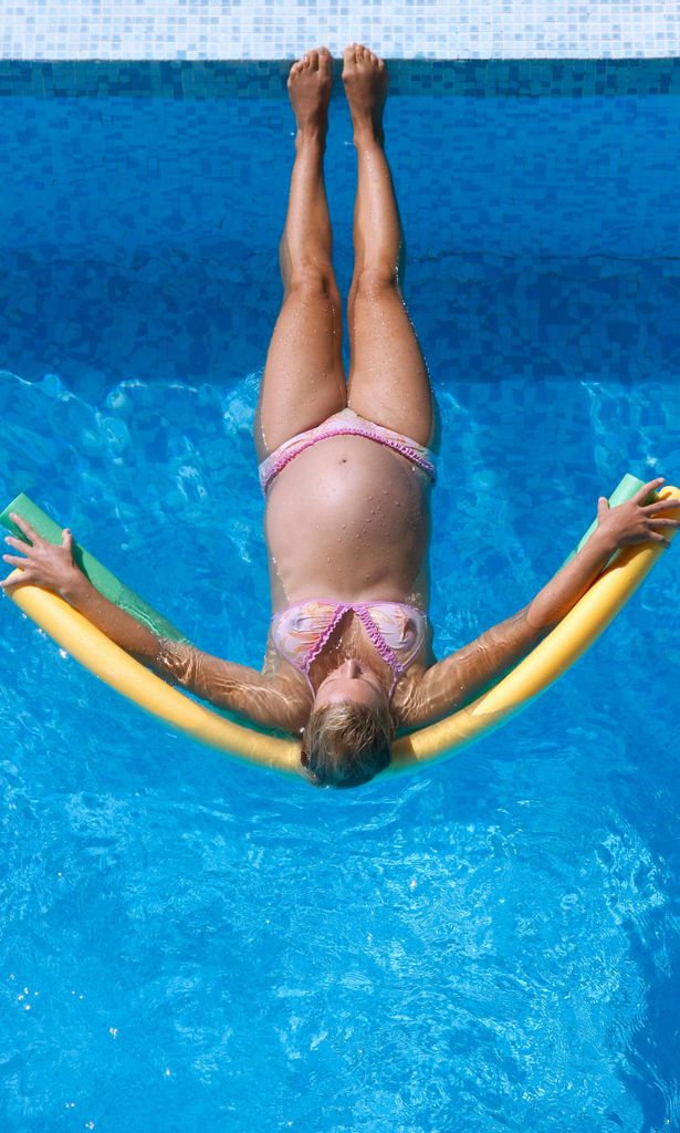 mujer en la piscina embarazada haciendo deporte con un churro bajo sus brazos y espalda