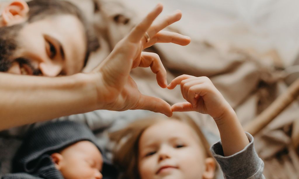 padre con sus hijas tumbado sobre la cama y haciendo un coraz n con sus manos