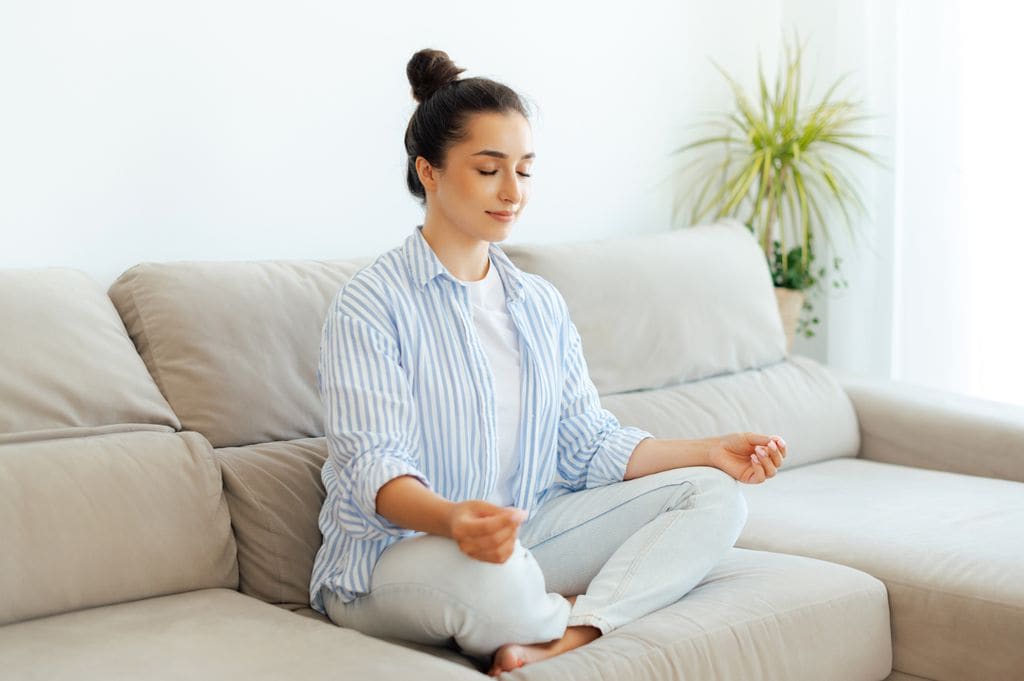 mujer meditando en casa, sentada en el sofá