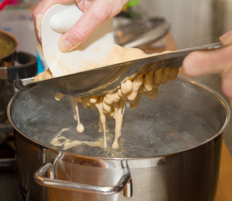 Echando la pasta de 'spaetzel' a un cazo con agua hirviendo para cocerlos.