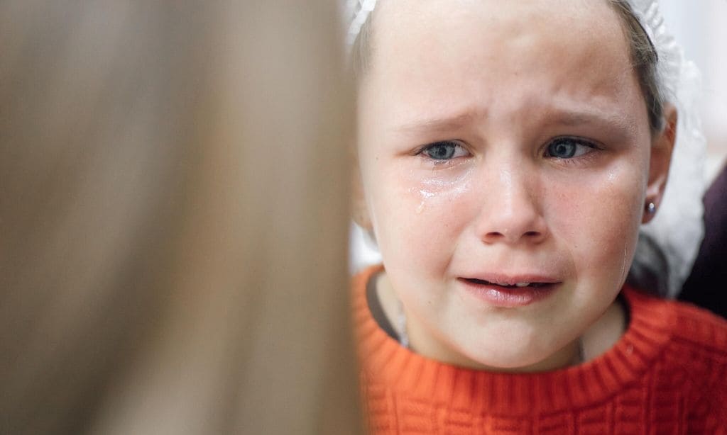 Portrait of little tearful girl in medical disposable cap crying in pain after ear piercing or other medical procedures in hospital office