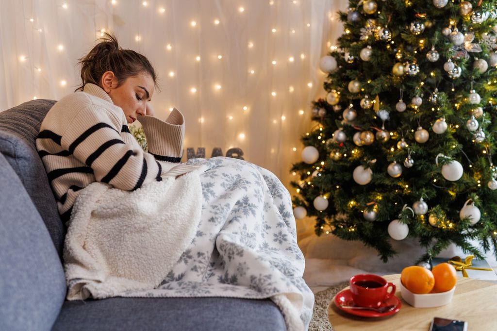 mujer triste sentada en el sofá junto al árbol de Navidad