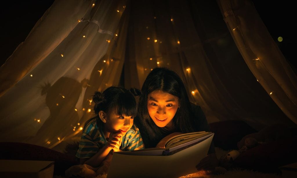 madre e hija leyendo cuento en casa con una carpa con luces