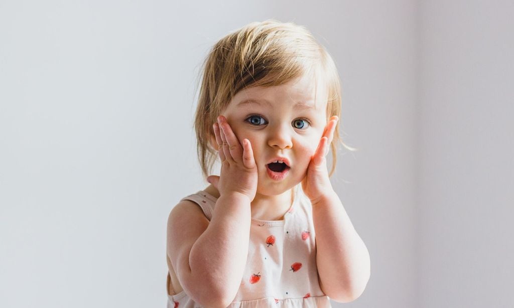 Surprised shocked child toddler girl with hands on her cheeks isolated on light background