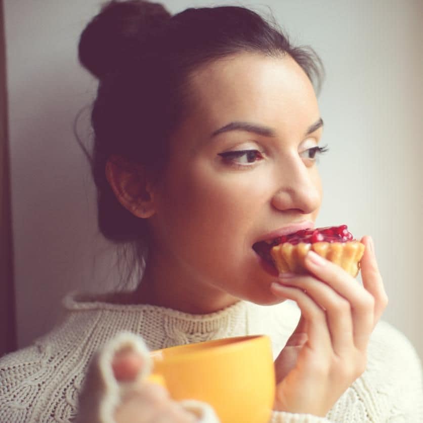 Joven abrigada comiendo cupcake con taza de café en mano