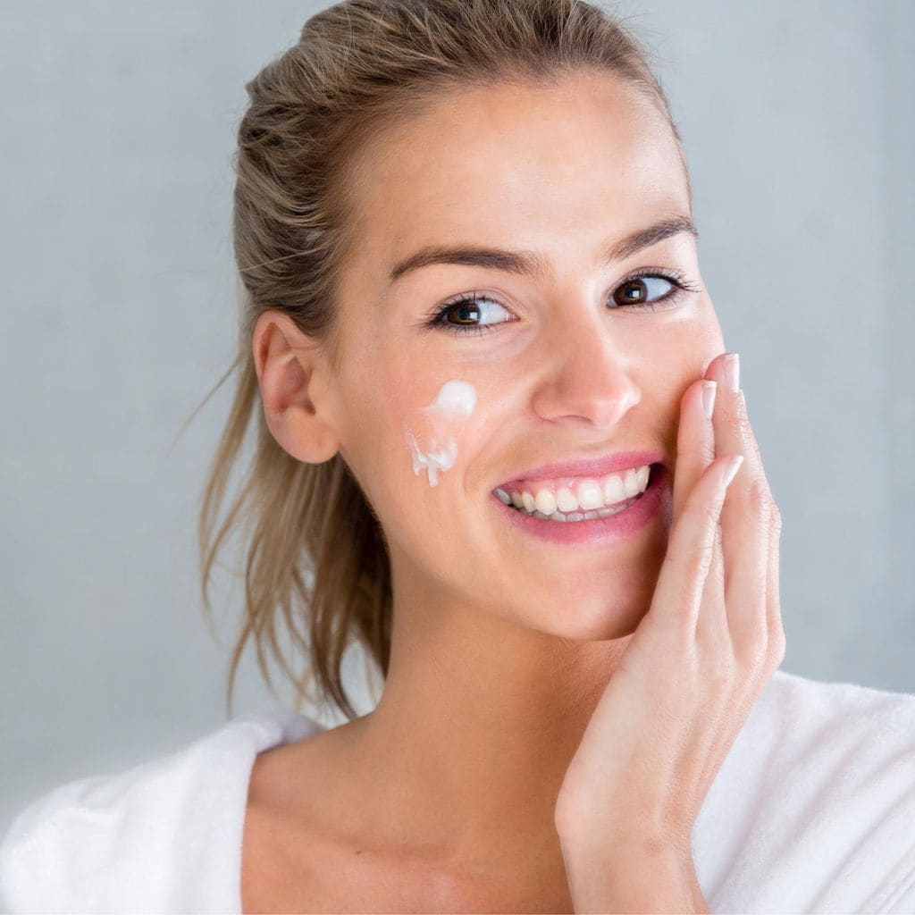 mujer joven aplica crema hidratante en su rostro