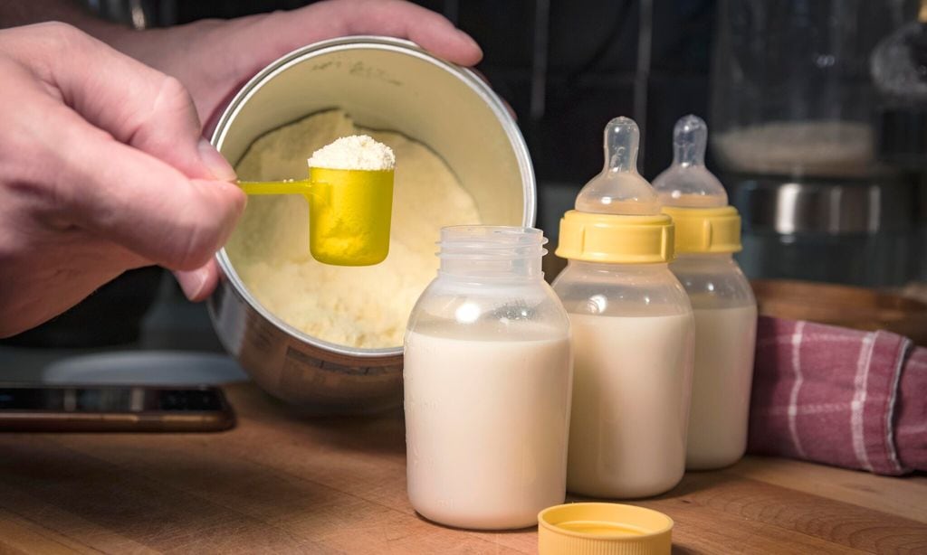 Hand holding scoop of powdered baby formula, ready to mix in bottles