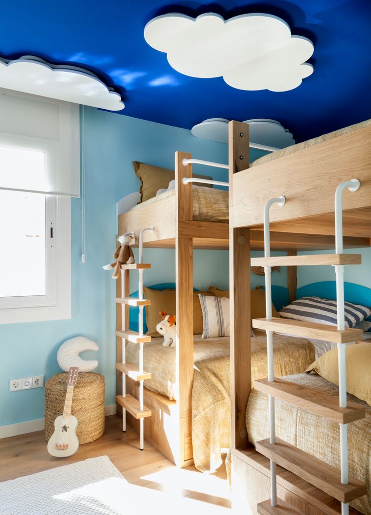 Dormitorio infantil con literas y techo azul con nubes.