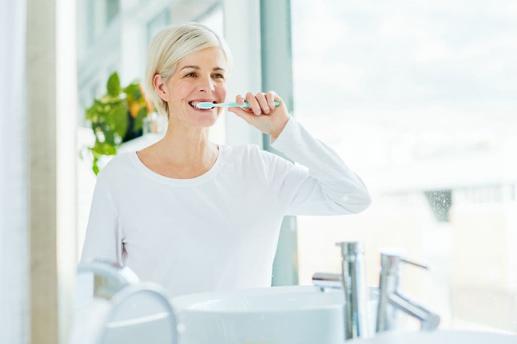 mujer madura lavándose los dientes en el cuarto de baño