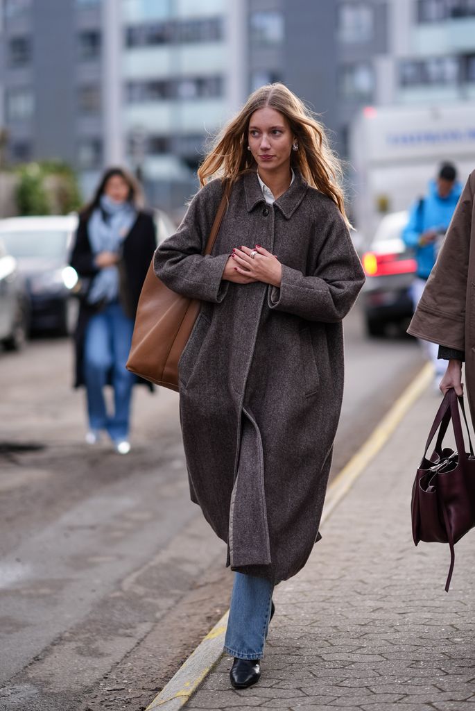 Una invitada lleva un bolso grande de cuero marrón, un abrigo largo de invierno gris, pantalones vaqueros azules, zapatos de cuero puntiagudos, fuera de Skall Studio, durante la Semana de la Moda de Copenhague AW24 el 31 de enero de 2024 en Copenhague, Dinamarca.