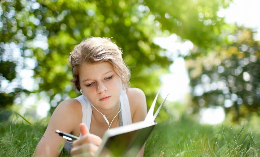 a young girl listening to music and studying in the park