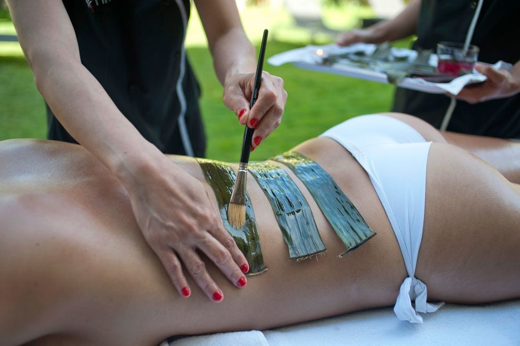 Mujer aplicando aceite en hojas de platanera para el masaje hilot