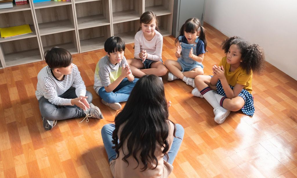 asian female teacher and group of multiethnic elementary school pupils singing together