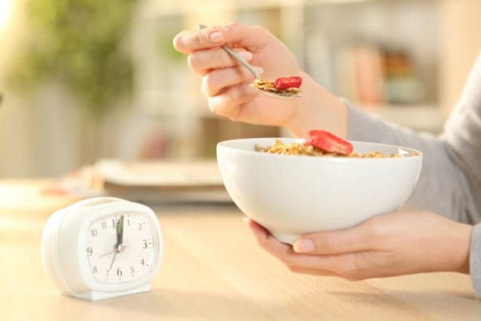 mujer comiendo con un reloj cerca