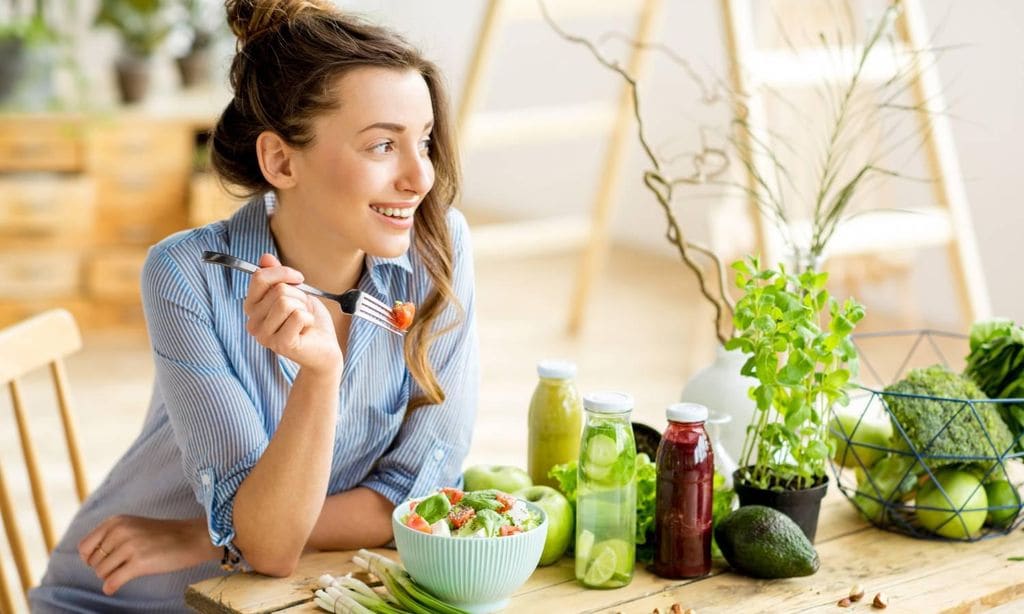 mujer comiendo plato de verduras sentada en una mesa feliz