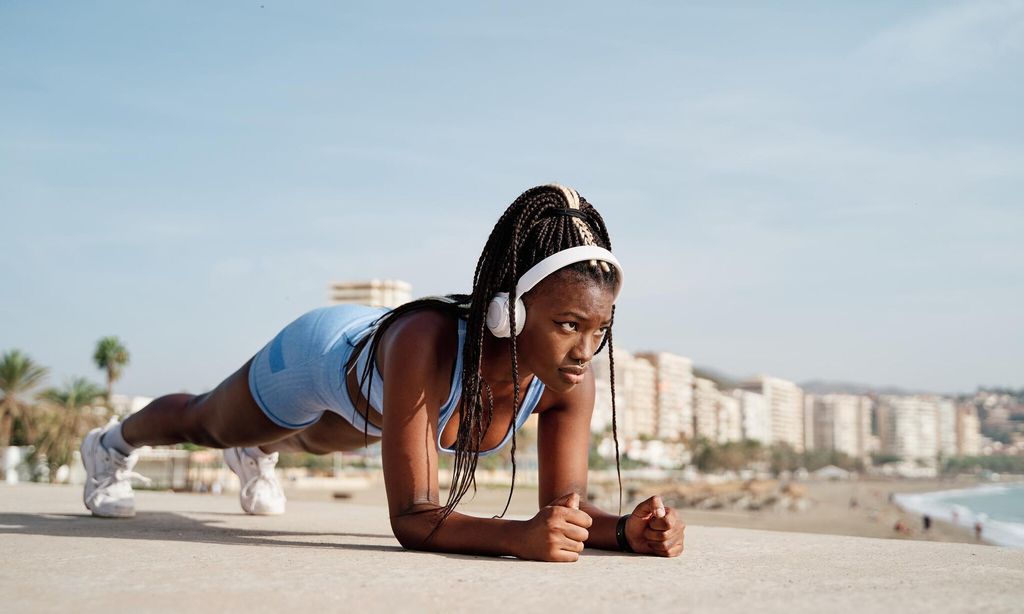 Young black female athlete focused on doing plank on her arms on a stone wall. Concept of sport and African American ethnicity.