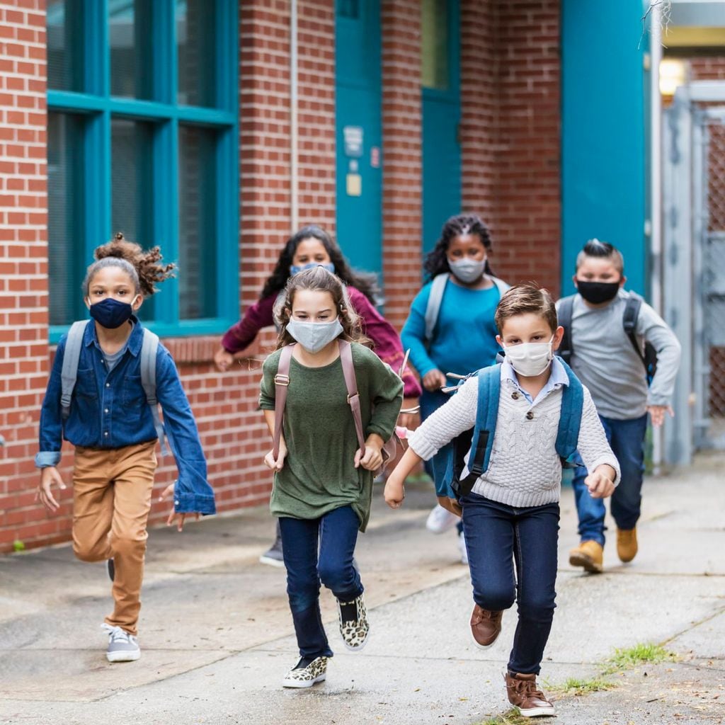 School children with face masks running outside building