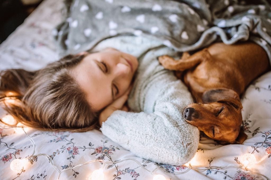 Mujer durmiendo en su cama con un perro con luces de Navidad