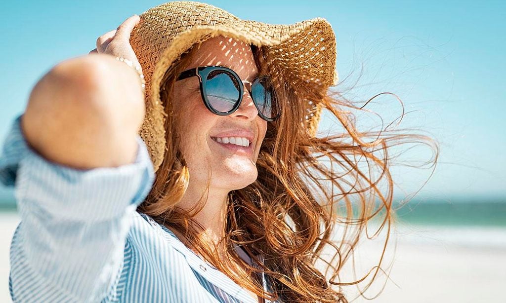 Mujer con sombrero y lentes de sol en la playa