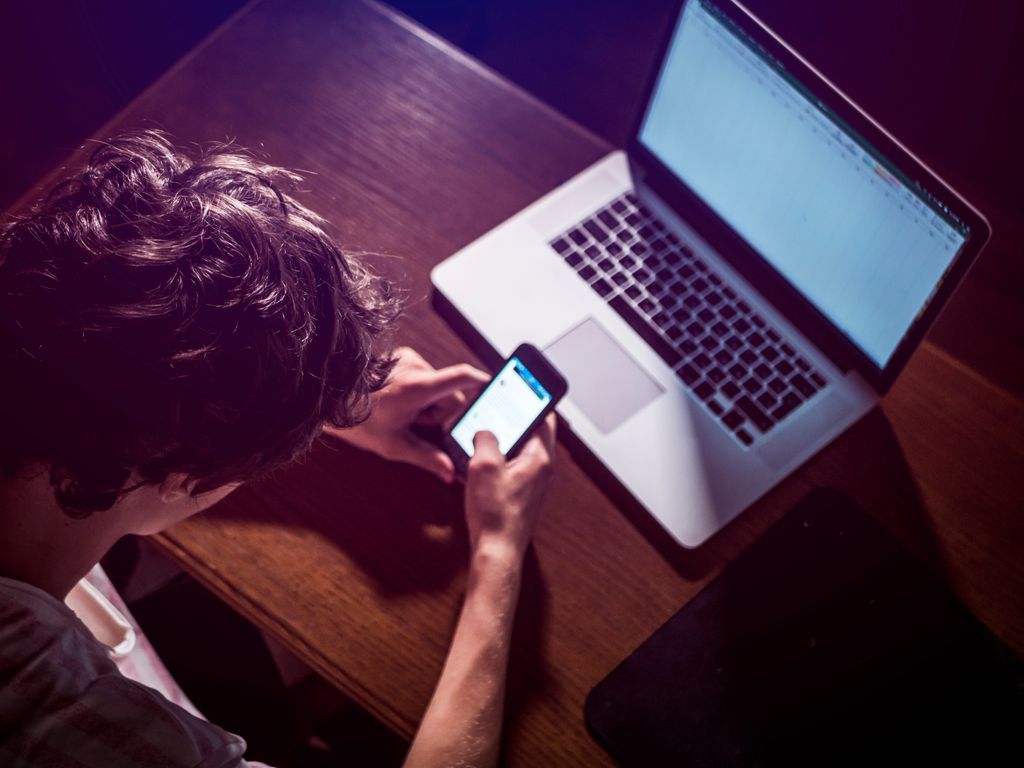 Adolescente viendo a la vez el móvil y el ordenador