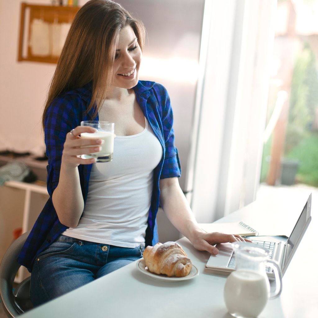 mujer tomando leche y trabajando de su casa