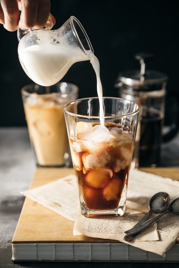 Persona virtiendo espumador de leche sobre un vaso con café y hielos