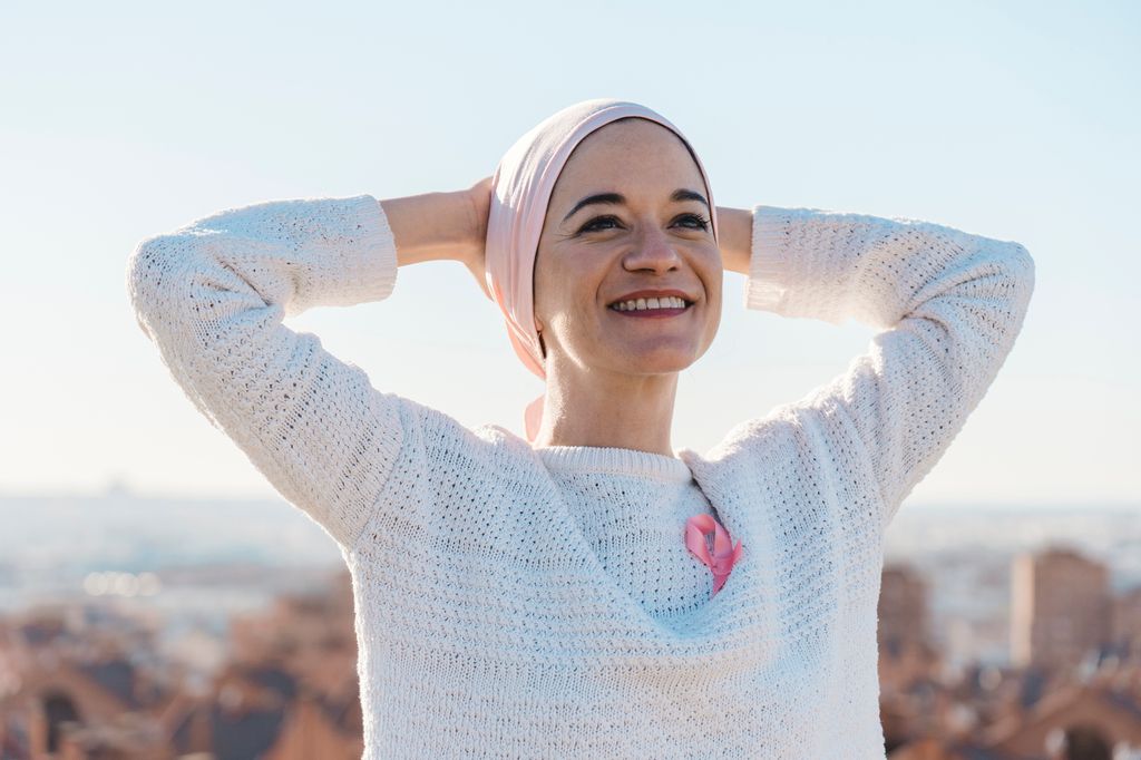 mujer sonriente con cáncer, con un pañuelo cubriéndole la cabeza y un lazo rosa