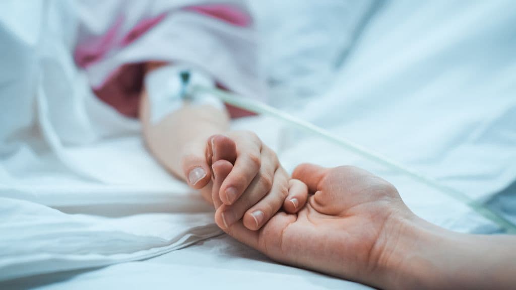 Madre dando la mano a su hijo con un suero en el hospital