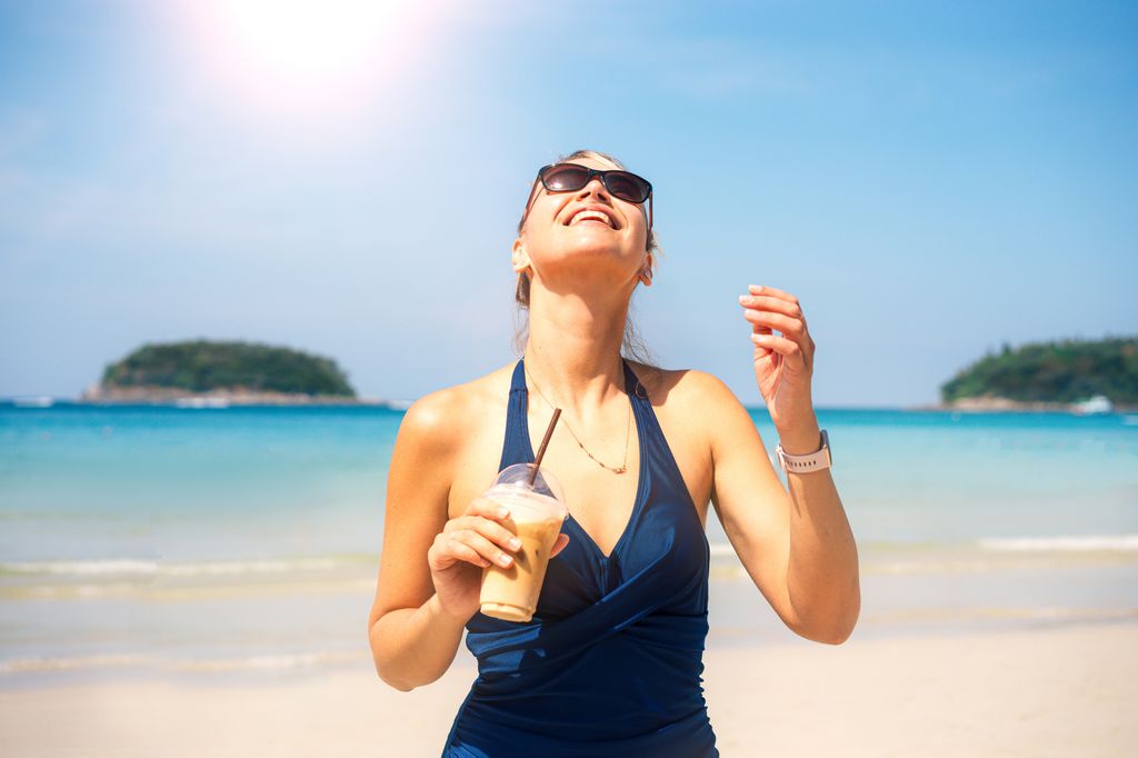 Mujer feliz disfrutando de una bebida helada  durante las vacaciones de verano en una playa tropical.