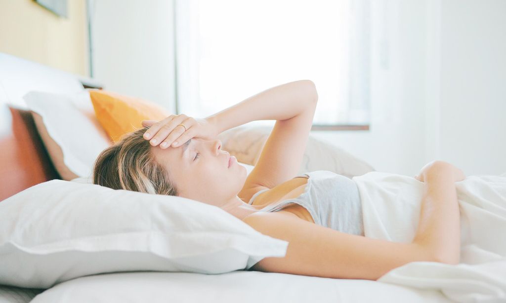 mujer tumbada en la cama con la mano en la frente